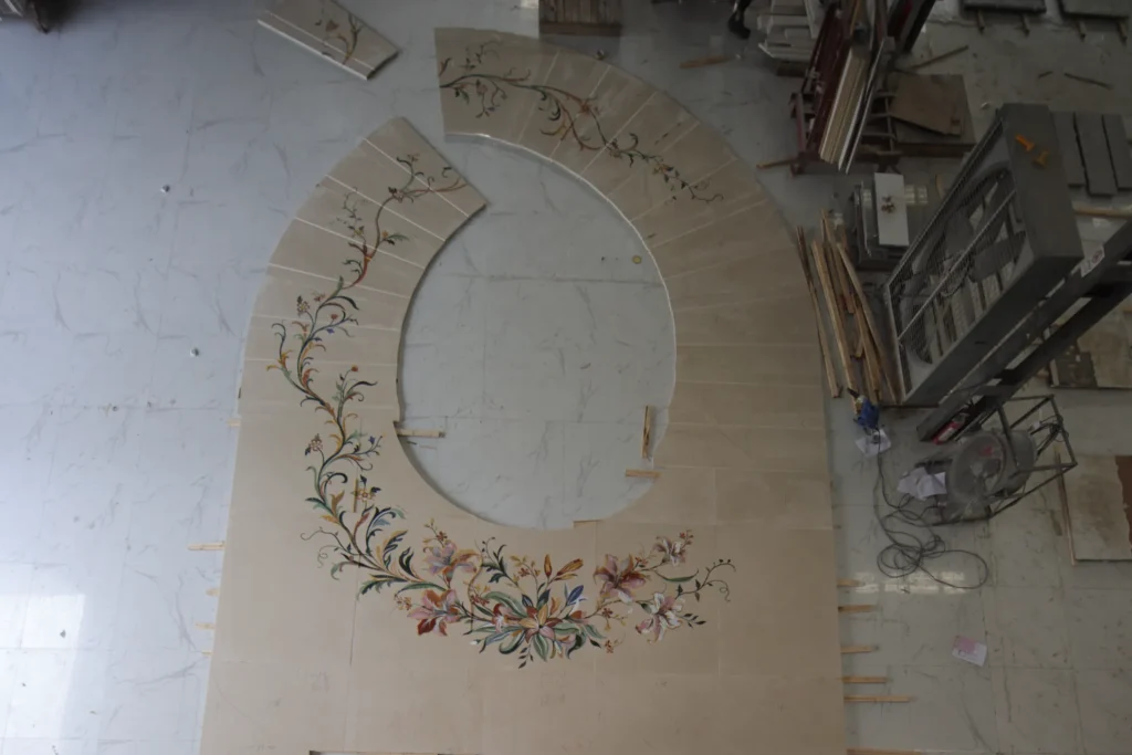 Curved marble inlay panel with floral pietre dure motif in a workshop.