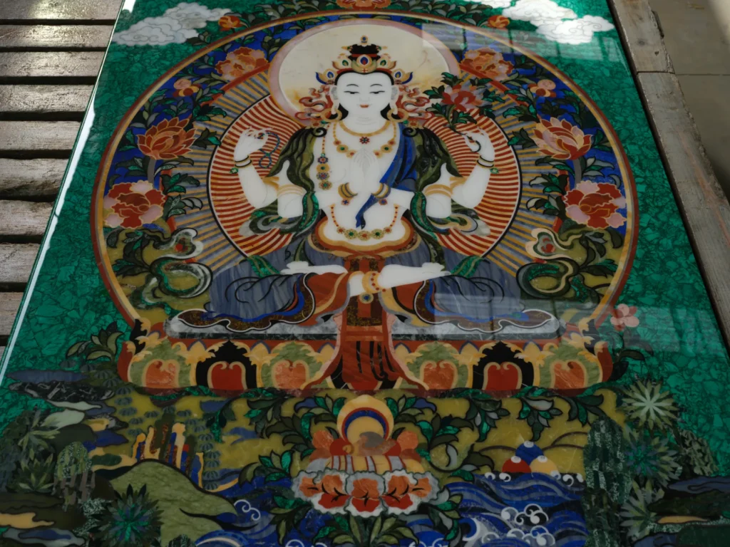 Marble inlay panel depicting a white multi-armed deity seated on a lotus within an ornate floral mandorla.
