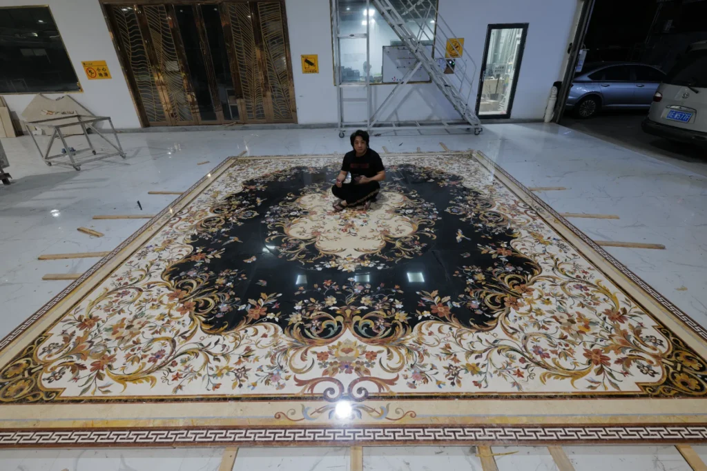 Large rectangular marble inlay with floral scrollwork and a central medallion on a dark ground, displayed in a workshop.