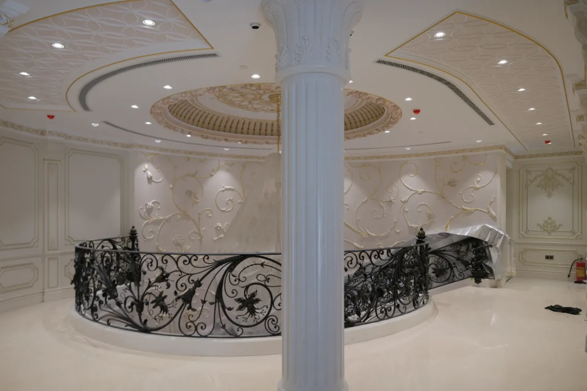 عمود رخامي أبيض وألواح جدارية مزخرفة في تصميم داخلي فخم مستدير مع درابزين حديدي أسود.