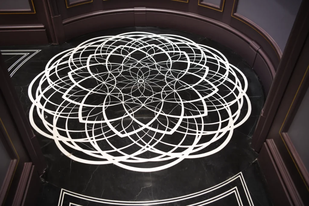 White geometric waterjet marble medallion inlaid into a polished black marble floor.