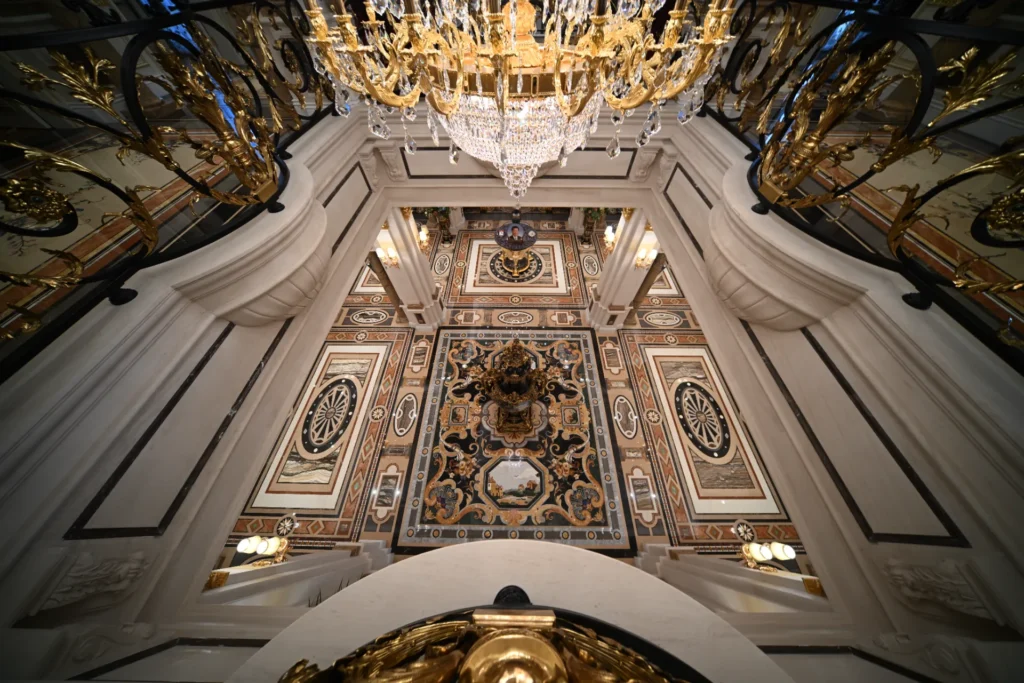 Ornate marble inlay floor with geometric medallions and pietre dure details beneath a gold chandelier.