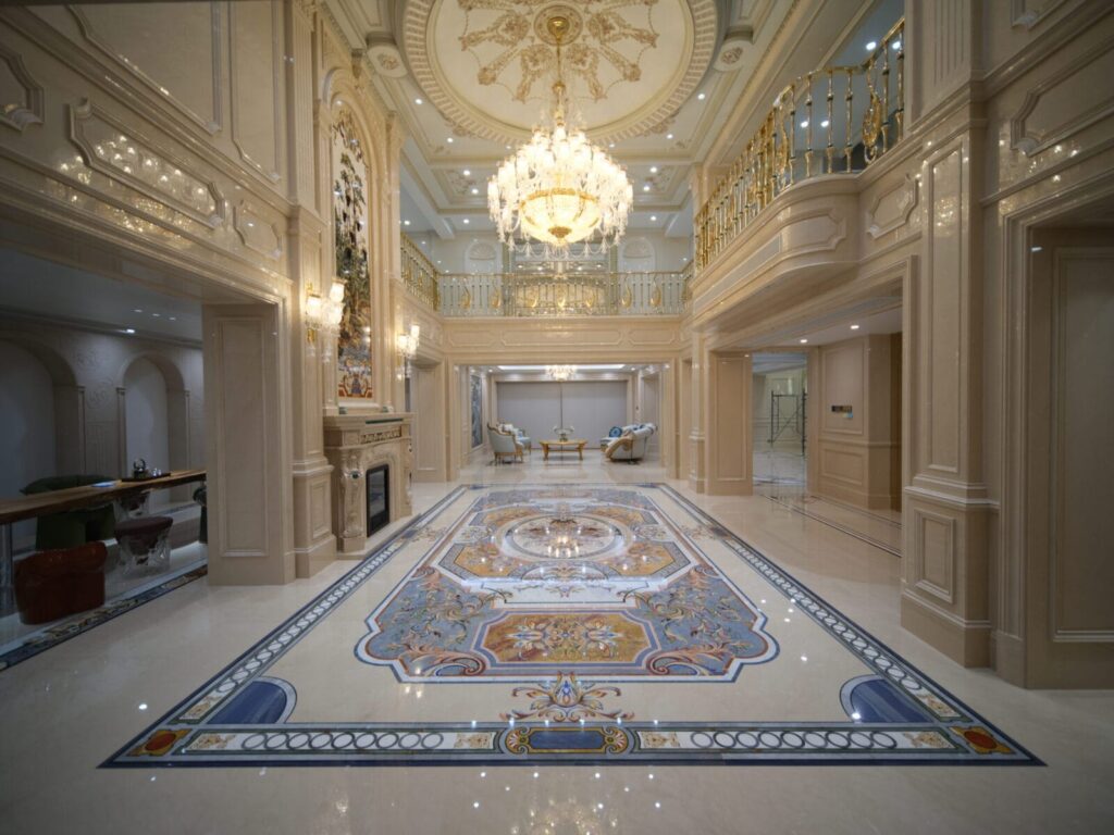 Large marble inlay floor medallion with ornate blue and gold scrollwork in a luxury foyer.
