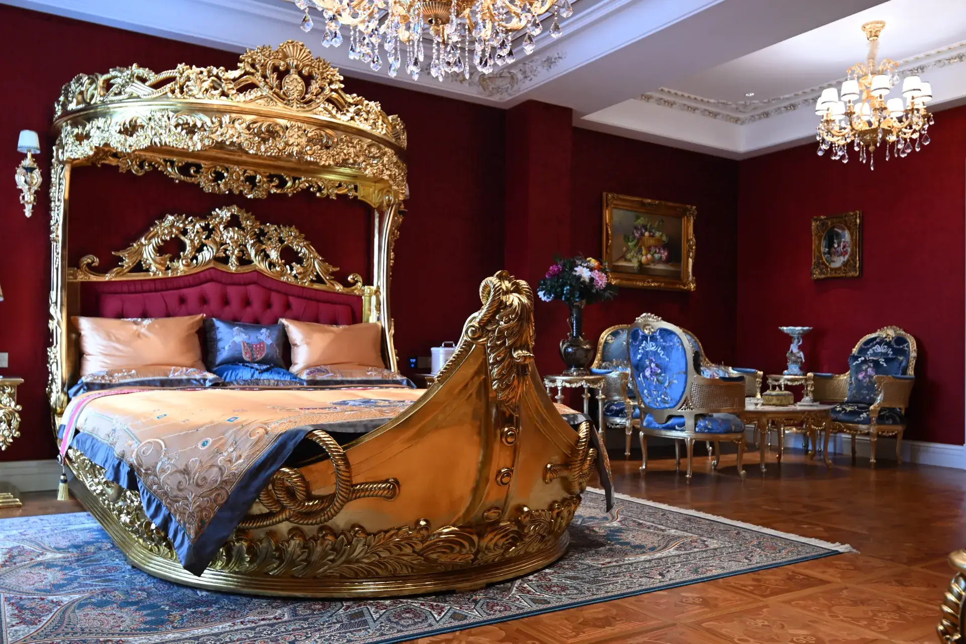 Luxury bedroom in Mongolia with ornate, gold-toned bed frame, red walls, and chandelier lighting.
